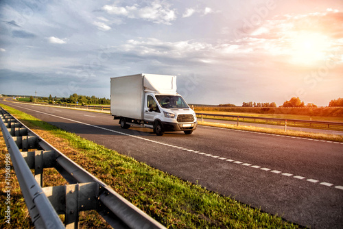 A white light-duty van isotherm transports products between cities on a country road in summer, sunset, industry photo