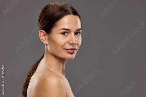 Portrait of elegant, beautiful, tender young woman with ponytail, smooth, clear face without makeup against studio background. Concept of natural beauty, cosmetology and cosmetics, skin care photo