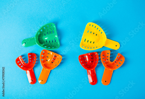 Multi-colored dental spoons for taking an impression of the dental jaw on a blue background. Making an impression of the jaw for braces and dental prosthetics, close-up. photo