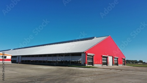 The barn is red in color. A building for keeping cows in winter in the cold season. Where cattle live on a dairy farm in winter. Red huge shed for animals. Red facade of a building made of metal struc