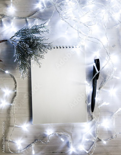 a notebook in a Christmas garland with a branch of a fir tree in silver color, a black pen. light background