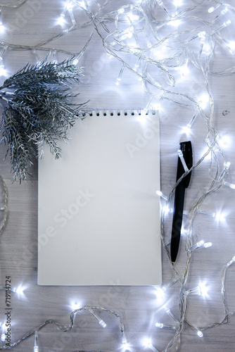 a notebook in a Christmas garland with a branch of a fir tree in silver color, a black pen. light background