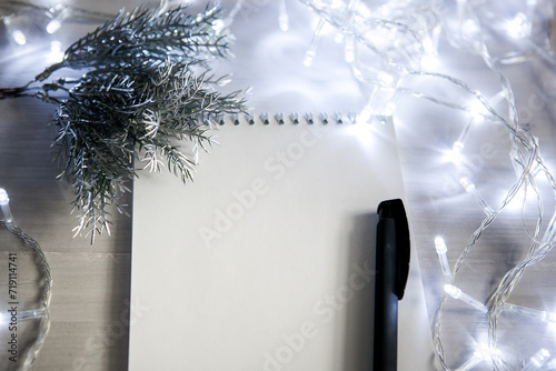 a notebook in a Christmas garland with a branch of a fir tree in silver color, a black pen. light background