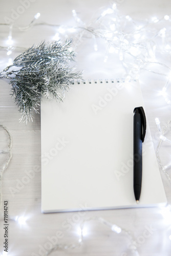 a notebook in a Christmas garland with a branch of a fir tree in silver color, a black pen. light background