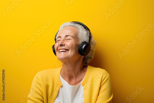 happy senior woman in headphones listening to music on yellow background with copy space. Hipster. Music Streaming Service Concept with Copy Space.