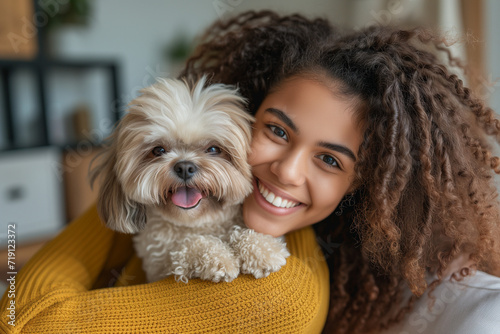 Happy curly-haired woman hugging her shih tzu dog in a living room