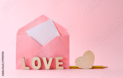 Pink envelope with letters and wooden heart on pink background