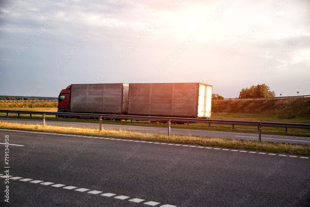 Obraz premium A truck with a semi-trailer and a hitch transports cargo against the backdrop of a field along the highway. Bulk cargo transportation concept, logistics company and business. Copy space for text