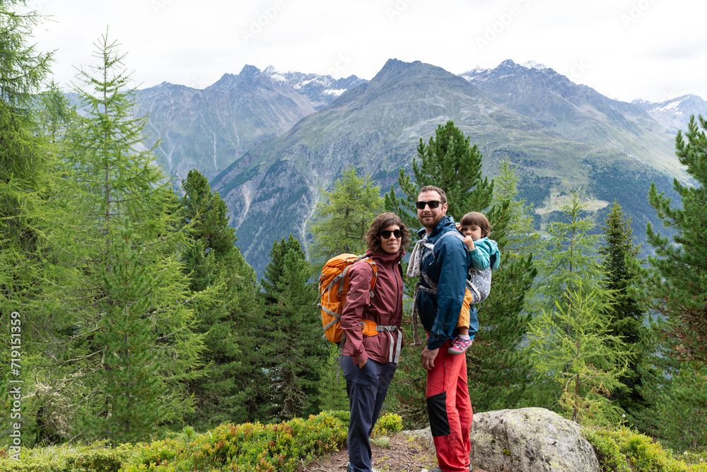 Portrait of a smiling family with their little daughter in a baby carrier at father's back during a hiking day in Sölden,  Austrian Alps.