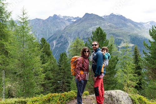 Portrait of a smiling family with their little daughter in a baby carrier at father's back during a hiking day in Sölden, Austrian Alps.