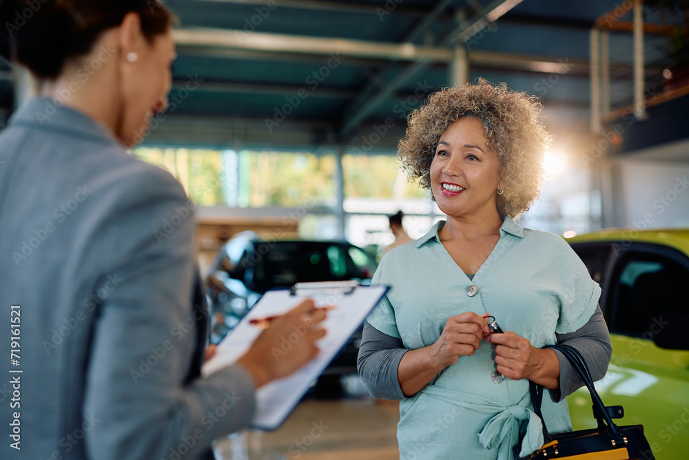 Happy mature woman talks to salesperson while buying new car in showroom.