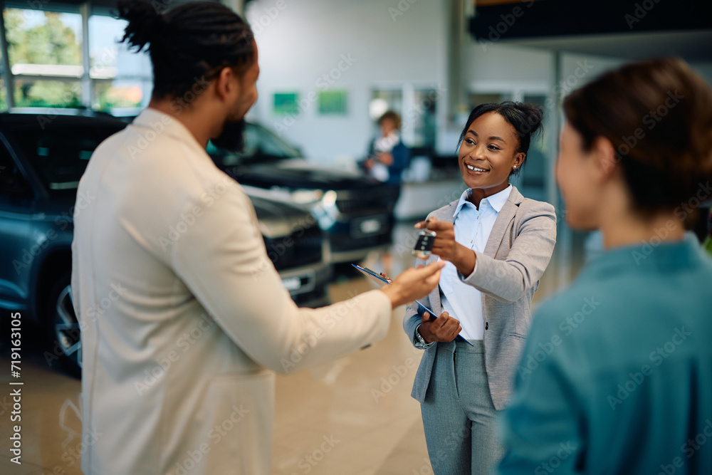 Happy black saleswoman giving to couple key of their new car in showroom. Happy black saleswoman giving to couple key of their new car in showroom.