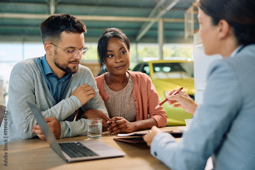 Young multiracial couple about to sign contract during meeting with car saleswoman in showroom. Young multiracial couple about to sign contract during meeting with car saleswoman in showroom.