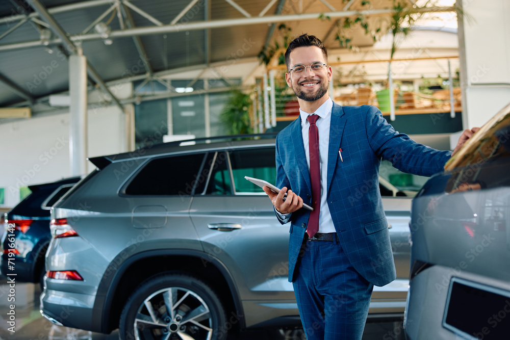 Young happy salesman working at car dealership and looking at camera. Young happy salesman working at car dealership and looking at camera.