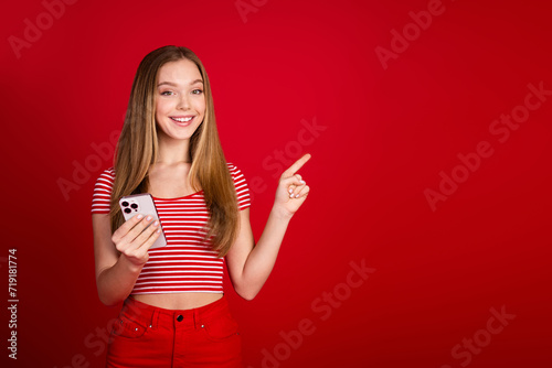 Photo of cute sweet girl wear striped top typing apple iphone samsung modern gadget pointing empty space isolated red color background