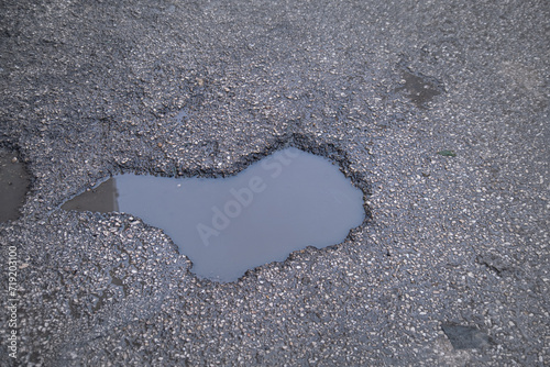 A water-filled hole on an asphalt street. It poses a danger to pedestrians, motorcycles and vehicles.