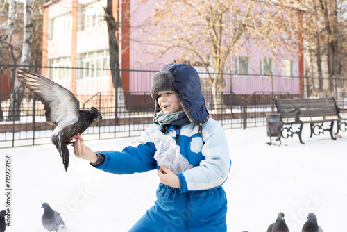 cute preschooler boy extends his hand forward to a flying wild pigeon on a winter day. A child walks on the street and interacts with birds with interest photo