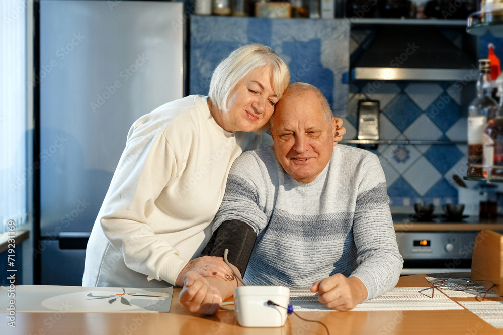 An elderly woman measures her husband's blood pressure and pulse.