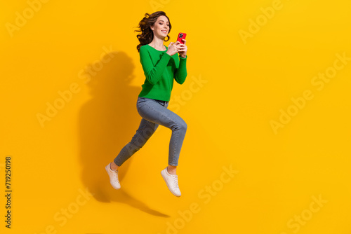 Full body length photo of jumping trampoline running with smartphone cant stop using her device isolated on yellow color background