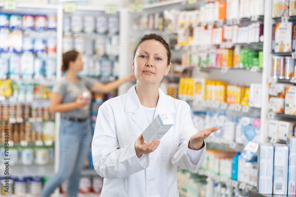 Adult female pharmacist in uniform posing with remedy while working in pharmacy
