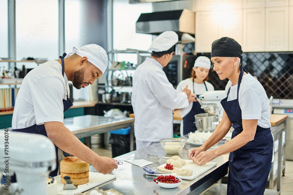 focus on diverse chefs working with dough, their blurred colleague and chief cook baking on backdrop focus on diverse chefs working with dough, their blurred colleague and chief cook baking on backdrop