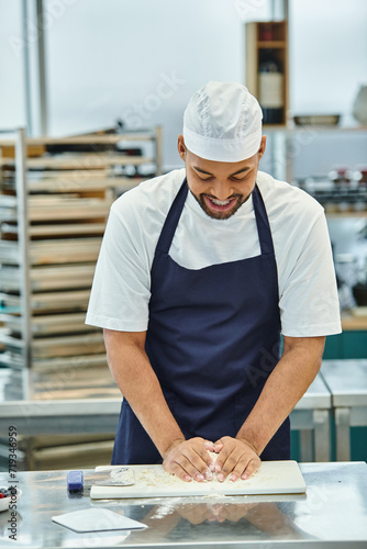 Fototapeta Naklejka Na Ścianę i Meble -  handsome joyous african american chef in apron with toque and braces working with dough attentively