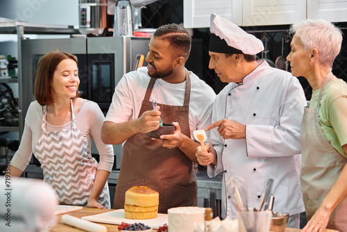 jolly young woman looking at her multiracial friends and chef, student brushing cake with syrup