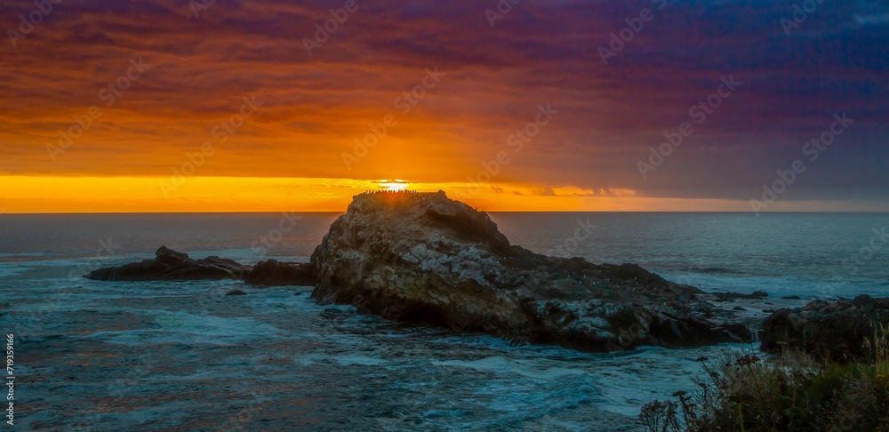 Sunset near Depoe Bay on the Oregon coast, with a flock of cormorants silhouetted on top of a sea stack in the forground