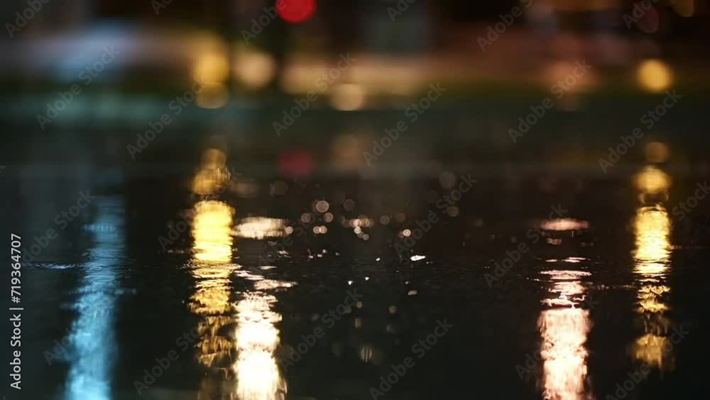 Atmospheric video of rainstorm in a night city. Heavy rain and splashes puddles taken from low point. Large drops break on the pavement in the light of street lamps. Slow motion
