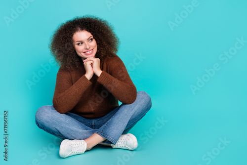 Full length photo of lovely young lady look interested empty space sit floor wear trendy brown garment isolated on cyan color background