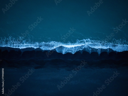 Majestic view of dark blue ocean waves splashing black sand beach, aerial top down shot. Dynamic background and natural beauty concepts.