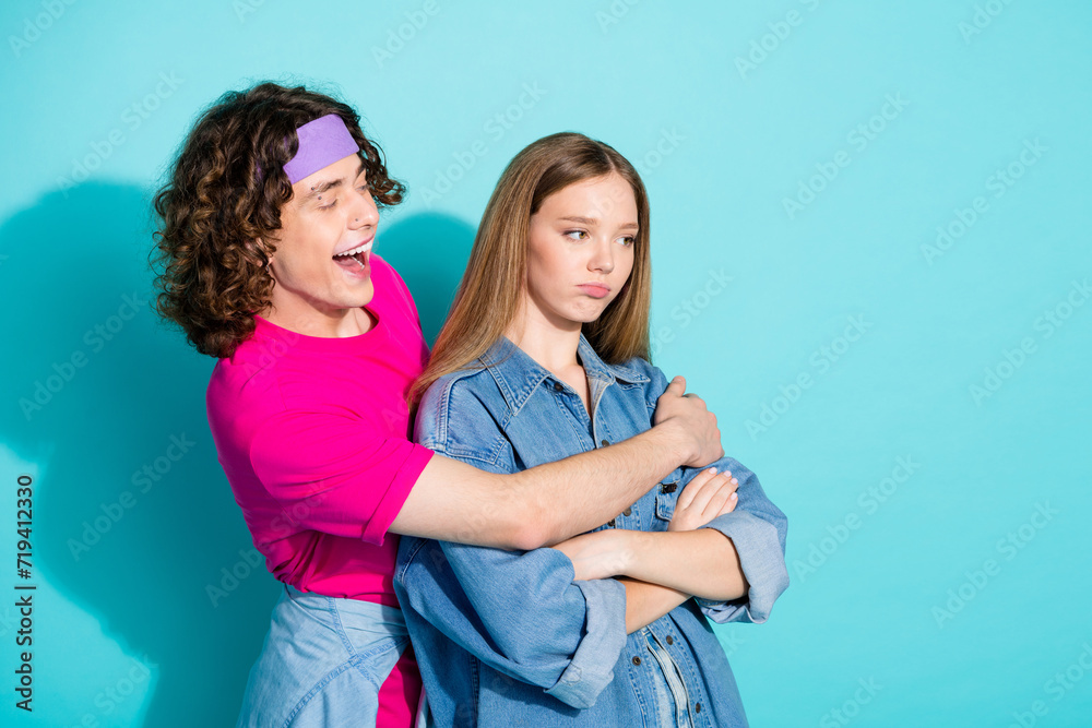 Photo of two funny youngsters teenagers girl seems offended when boyfriend in headband hugs isolated over aquamarine color background Photo of two funny youngsters teenagers girl seems offended when boyfriend in headband hugs isolated over aquamarine color background
