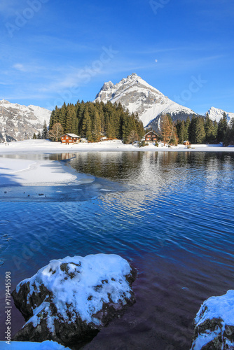 Winter landscape of the frozen Arni Lake with the snow-convered Alps peak Windgaellen at the background