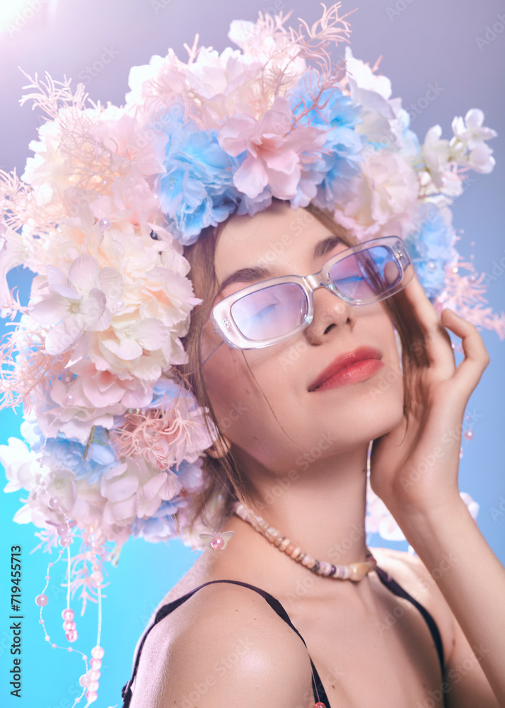 A charming woman in sunglasses and a flower wreath poses on a blue background
