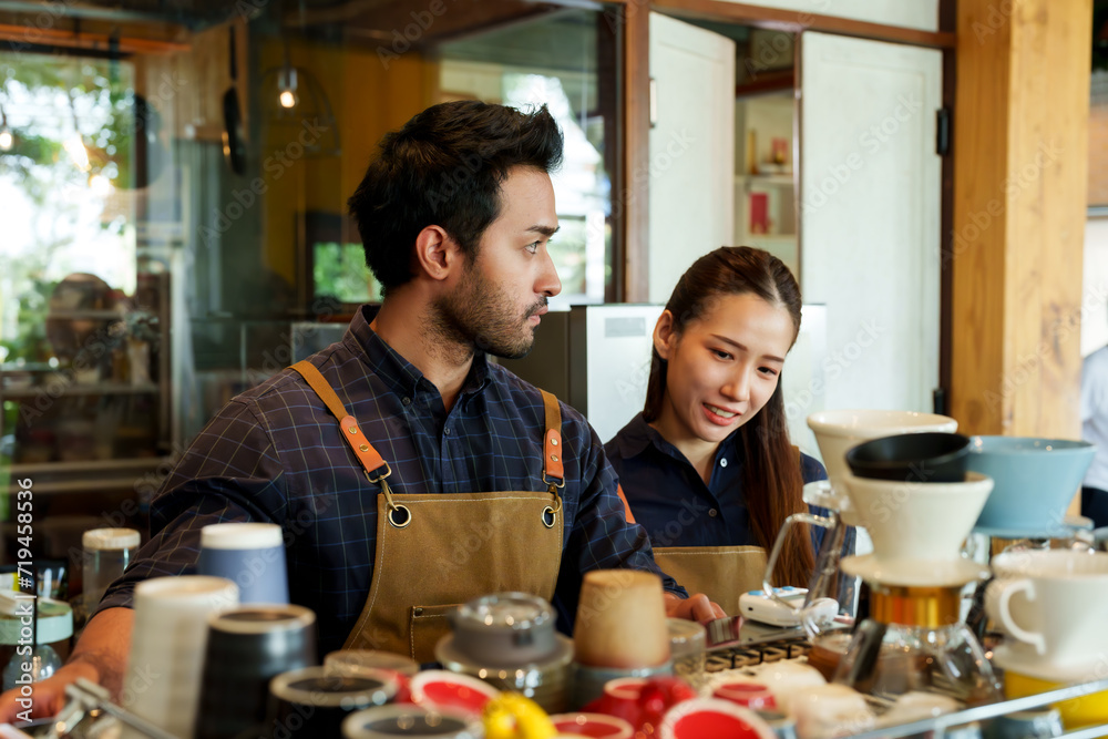 Young barista business couple, Indian male cafe owner teaching coffee making to Asian woman behind coffee machine counter. seemed interested and intent on learning how to make coffee at small cafe. Young barista business couple, Indian male cafe owner teaching coffee making to Asian woman behind coffee machine counter. seemed interested and intent on learning how to make coffee at small cafe.