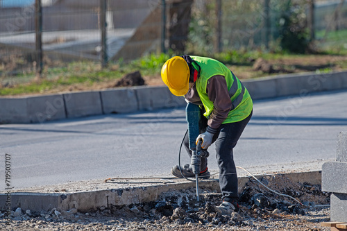 A man works with an air hammer on a road construction site.