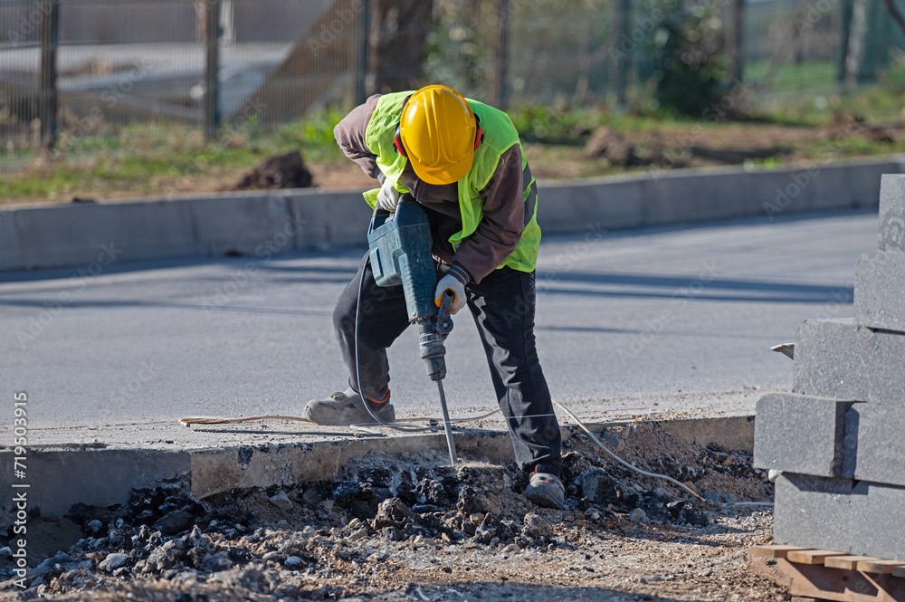 A man works with an air hammer on a road construction site. A man works with an air hammer on a road construction site.