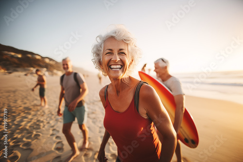 Laughing senior middle aged woman with gray hair and tattoos in sporty outfit walking on seaside beach with blurred aged friends in sunset. Aged people enjoy life. Active elderly people's lifestyle