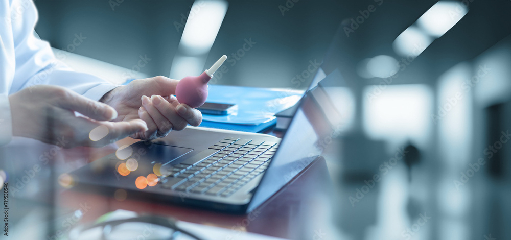Female doctor demonstrates enema in office with laptop computer. Female doctor demonstrates enema in office with laptop computer.