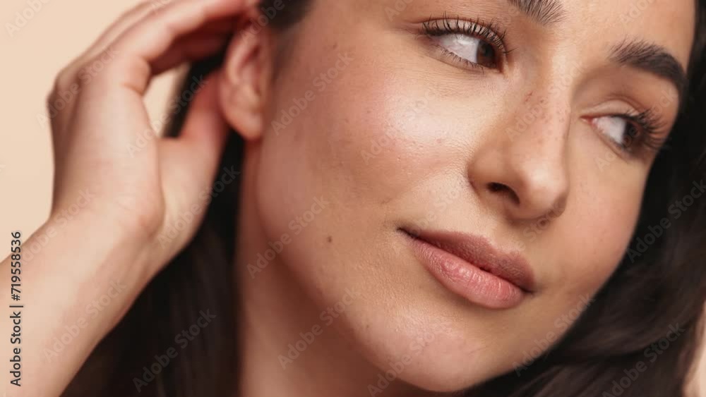 Close-up of a brunette woman touching her hair and face, showcasing clear skin and natural beauty. Perfect for representing skincare routines and beauty concepts.