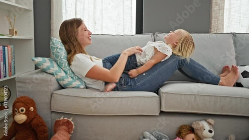 Happy caucasian mother and daughter tickling, playing on comfy sofa at home, lying, sharing relaxing family moments, laughing a lot photo