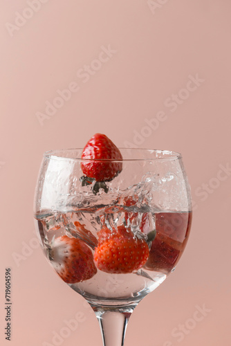 playing with strawberries in a glass with transparent liquid, uniform salmon color background
