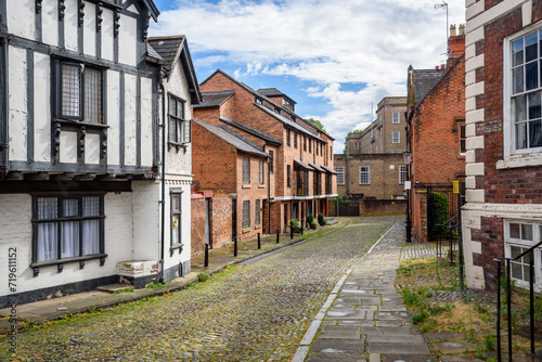 Empty cobbled street lined with brick houses in a city centre on a partly cloudy summer day