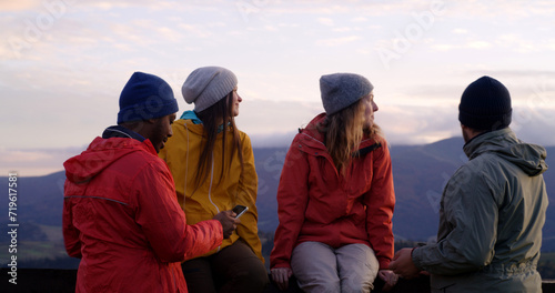 Hiking buddies stand near wooden fence and look at sunset. Group of diverse tourists or travelers enjoy the mountains landscape and beautiful nature during trip. Outdoor enthusiasts. Slow motion.