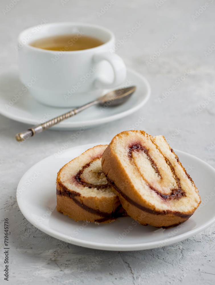 Roll with berry jam and chocolate in a cut with a cup of tea on a light background. Roll with berry jam and chocolate in a cut with a cup of tea on a light background.