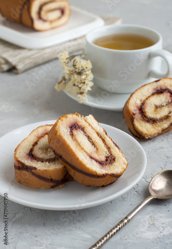 Roll with berry jam and chocolate whole and cut with a cup of tea on a light background. Close, free space.