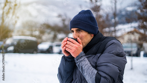 Hispanic handsome young man holding hot coffee or tea in snowy lanscape