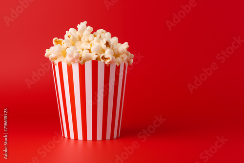 Delicious homemade popcorn in striped bucket cup on a red background AI Generation
