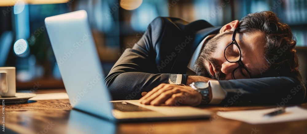 Tired overworked businessman sleeping over a laptop in a desk at job in his office. Copy space image. Place for adding text - obrazy, fototapety, plakaty 