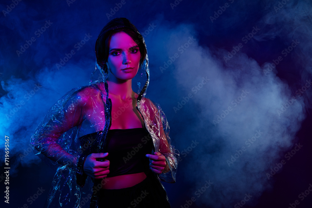 Photo of attractive girl stand pose touch transparent rain protective jacket on empty space mist dark blue background